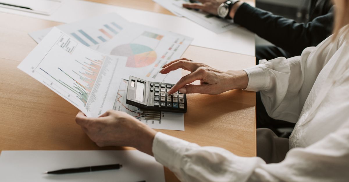 Hands performing financial calculations with charts and a calculator at a meeting table.