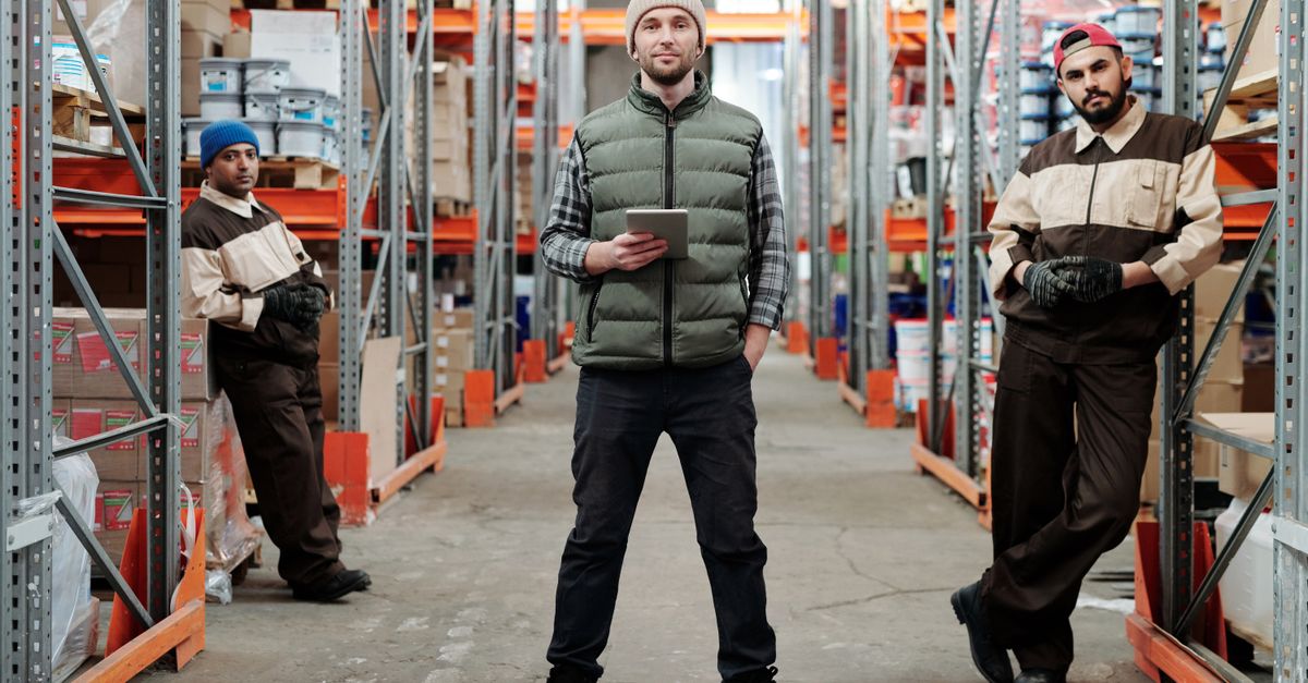 Three men in a warehouse standing among shelves with inventory.
