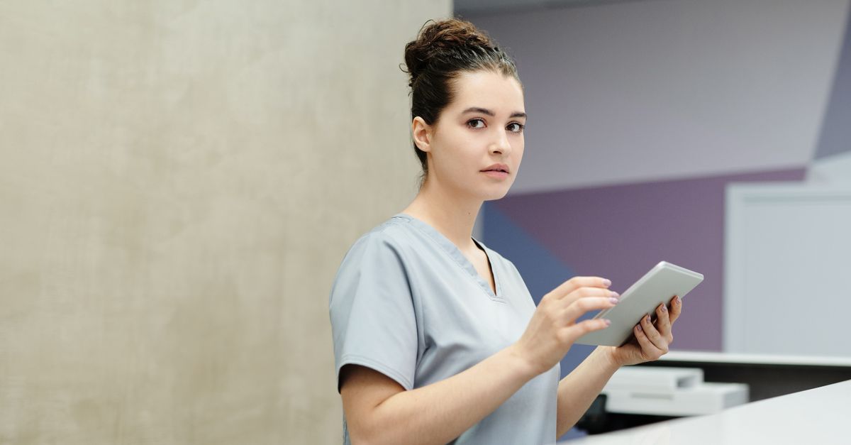 Professional receptionist using a tablet device at a modern office reception desk.