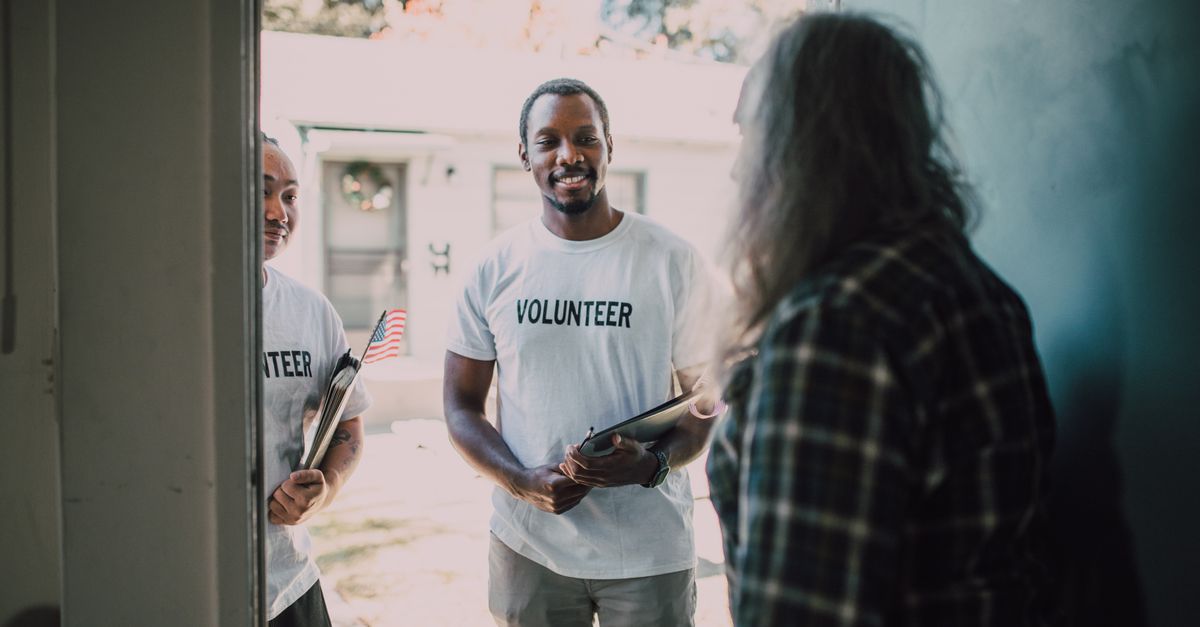 Two diverse volunteers, holding documents, visit a home to offer community support and services.