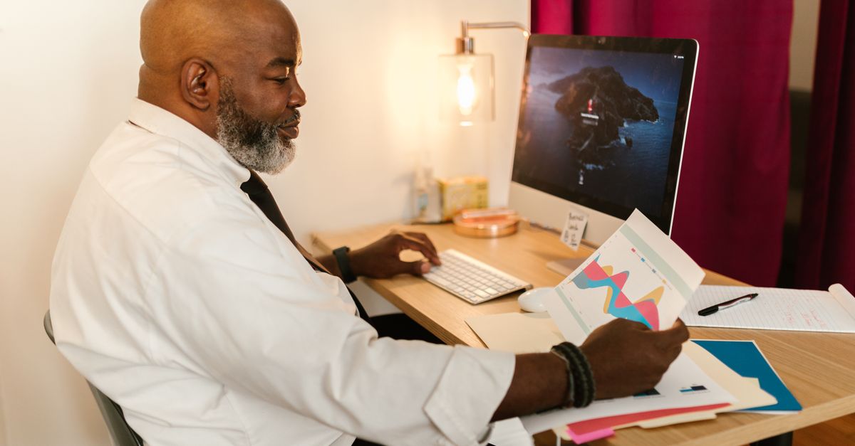 A mature professional working on business charts at a desk with a computer in an office setting.