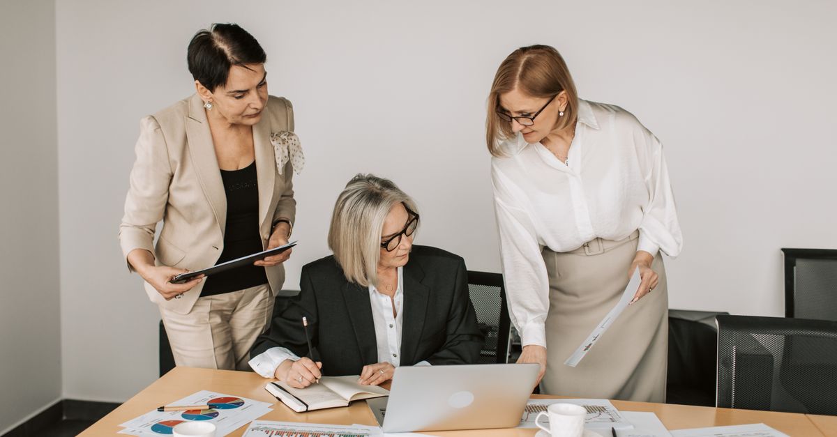 Three businesswomen discussing documents during a meeting in a modern office setting.