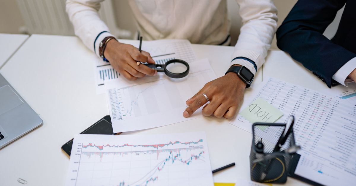 Business professionals reviewing charts with a magnifying glass in an office setting.