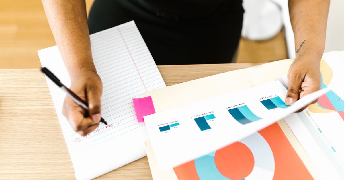 Businesswoman writing notes while analyzing printed graph reports at a desk.