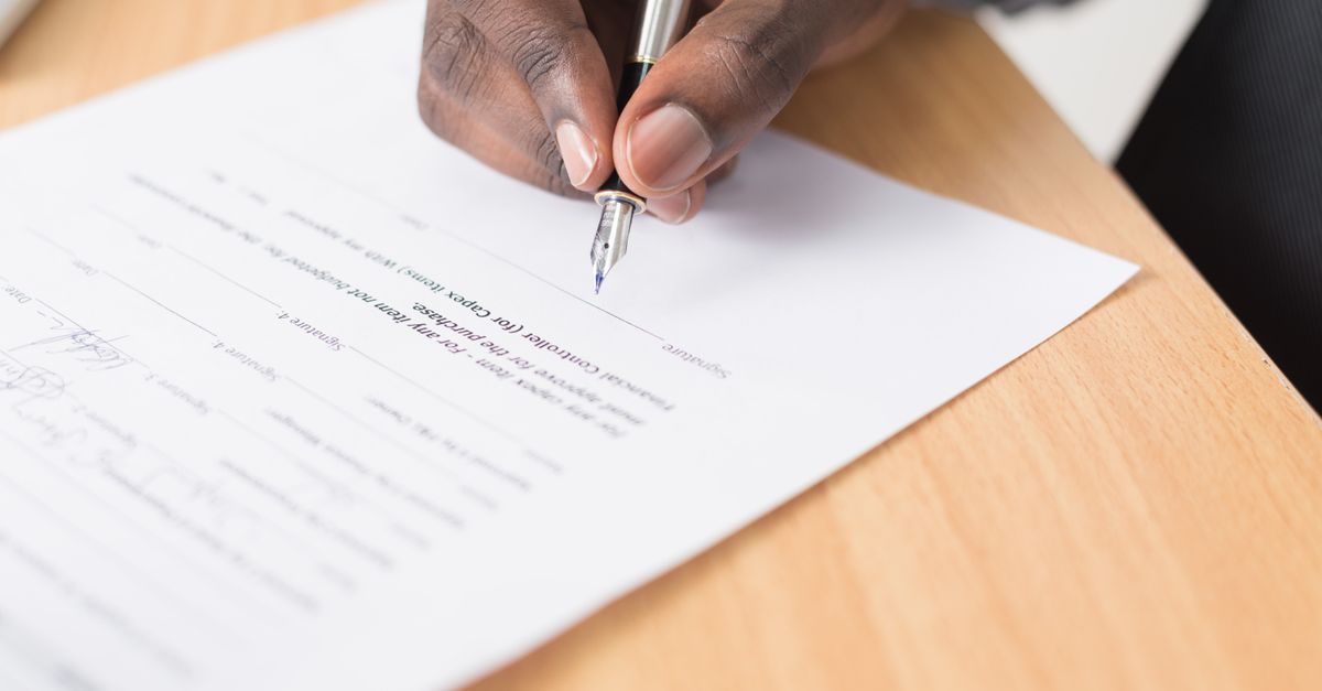 A hand holding a pen signing a document close-up on a desk, symbolizing agreement or contract finalization.
