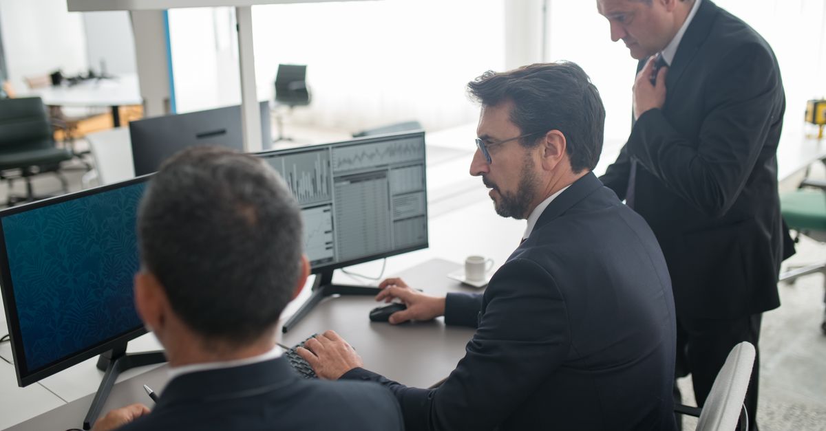 Colleagues in a modern office reviewing stock market trends and data on multiple screens.