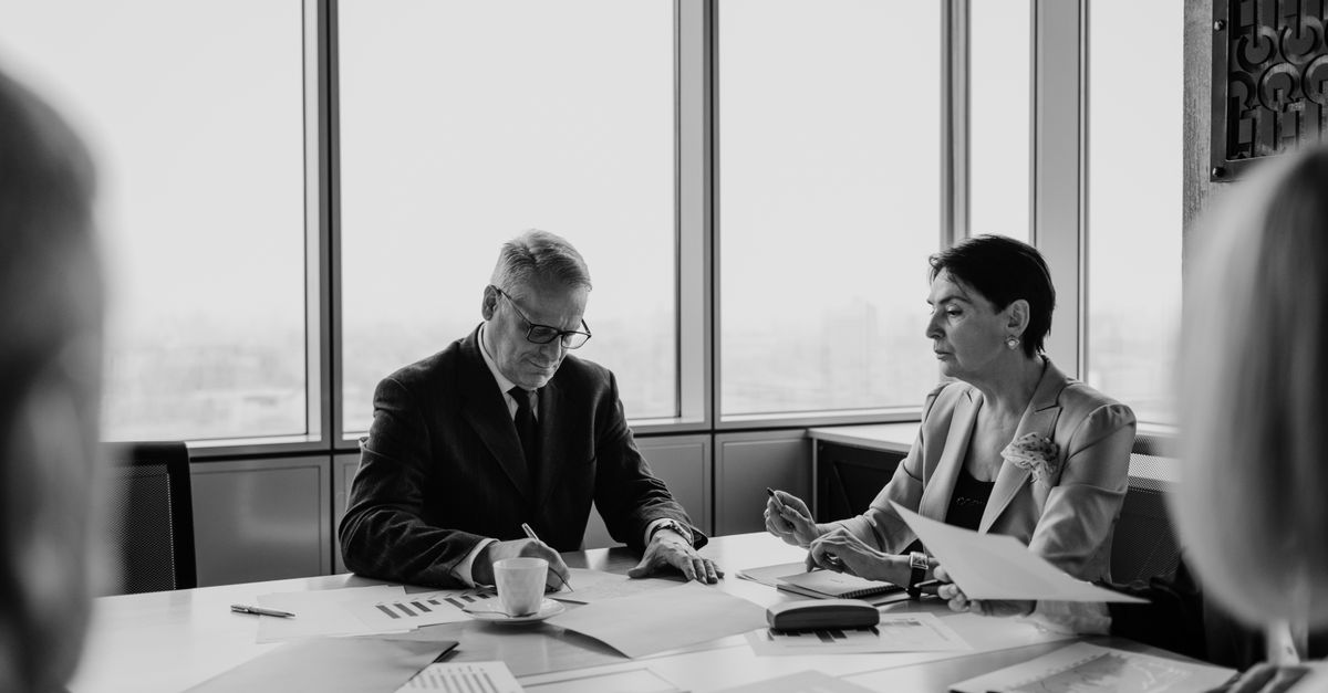 Black and white image of a business meeting with diverse professionals collaborating.